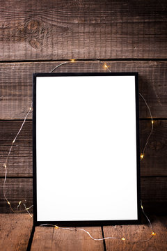 Empty   black  frame with twinkle light  on  aged wooden background.
