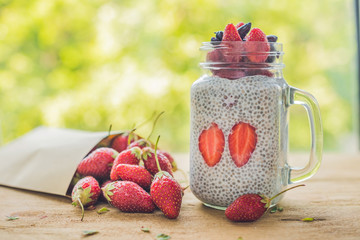 Healthy layered dessert with chia pudding, strawberry and honeysuckle in a mason jar on rustic...