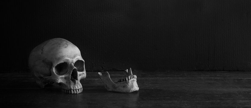 Skeleton skull head and jaw on old brown wooden table in the morgue with dim light