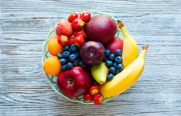 Bowl of fresh fruit with banana, apple, strawberries, apricots, blueberries, plums, whole grains, forks, top view - Powered by Adobe