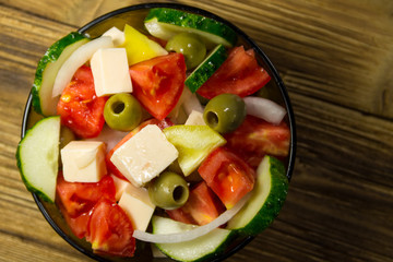 Greek salad in glass bowl on wooden table
