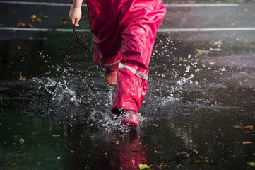 Children play on the street after the rain in pink bright rubber boots. The rays of the sun are reflected in the drops of water