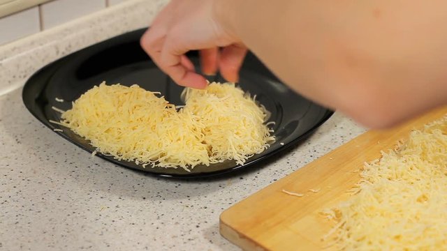 female hand shifts are fresh grated cheese in a plate. Woman grating cheese. preparation of pizza