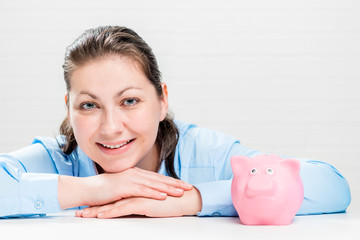Obraz na płótnie Canvas Beautiful young businesswoman in a blue shirt with a piggy bank on the table