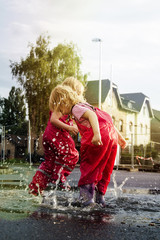 Children play on the street after the rain in pink bright rubber boots. The rays of the sun are reflected in the drops of water