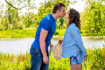 Fototapeta premium Pregnant woman and her husband kiss in the park near the lake