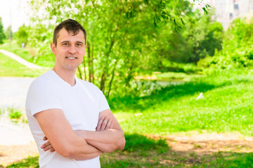 Naklejka na ściany i meble Horizontal portrait of a handsome man in a white T-shirt in the park
