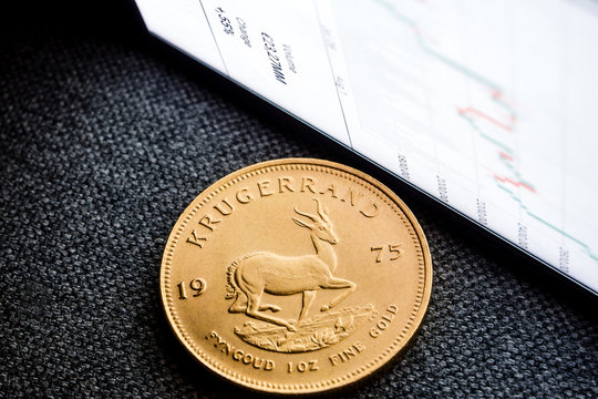 investing in golden coins / closeup of golden south african krugerrand coin with a chart reflection on close digital device with green and red bars