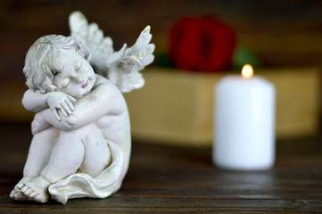 Angel, white candle and red rose on wooden background