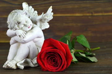 Angel and red rose on wooden background