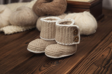 Fototapeta na wymiar winter knitted booties ang yarn on wooden background, warm winter or autumn background