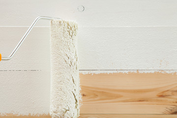 Paint roller brush with white paint on wooden background