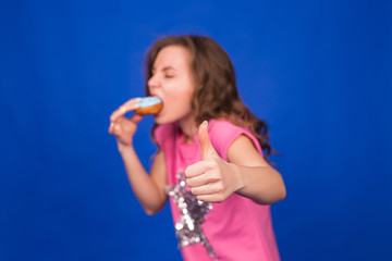 Young beautiful woman eating doughnuts on blue background. Unhealthy diet, junk food and food addiction concept