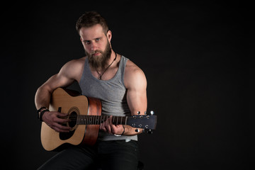 A charismatic man with a beard, playing an acoustic guitar, on a black isolated background. Horizontal frame