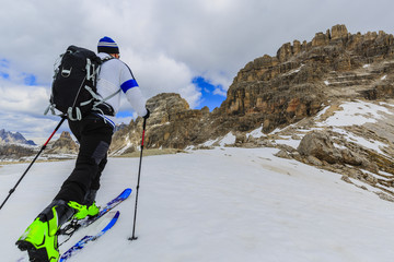 Mountaineer backcountry ski walking up along a snowy ridge with skis in the backpack. In background...