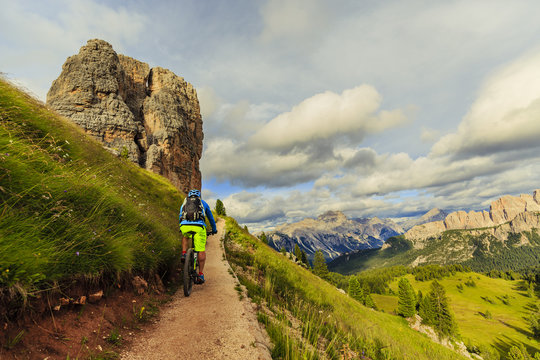 View of cyclist riding mountain bike on single trail in Dolomites, Cinque Torri, South Tirol, Italy