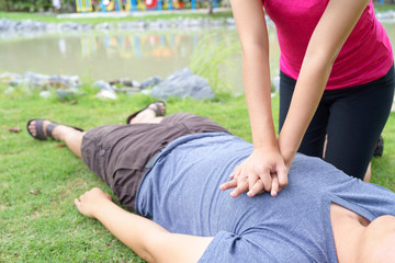 Woman giving cardiopulmonary resuscitation (CPR) to a man at public park.