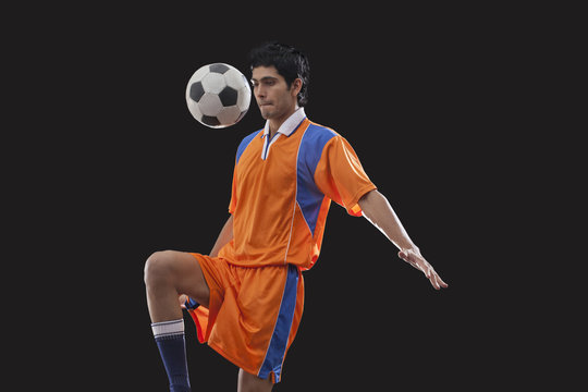 Male football player doing kick ups isolated over black background