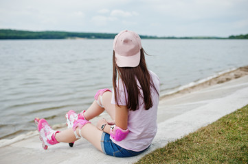 Portrait of a gorgeous young woman in casual clothes and cap sitting on the ground next to the lake.