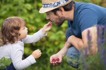 Adorable little baby girl and her father eating raspberries