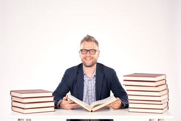 Portrait of middle-aged professor sitting at desk with book heaps on it