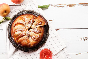Sweet pie with fresh summer peaches on white wooden distressed background with a glass of rose water. Harvest time concept. Horizontal composition with copy space viewed from above
