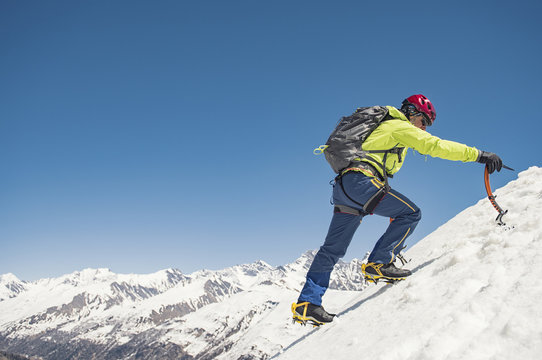 Hiker climbing on snowcapped mountain against blue sky