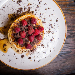 Top view Delicious pancakes with fresh raspberry, chocolate crumbs and maple syrup on the white round plate on the served for breakfast dark wooden table. close-up. selective focus.