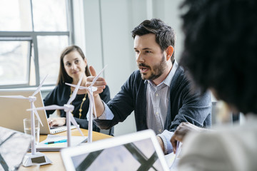 Businessman explaining wind turbine models to colleagues in office