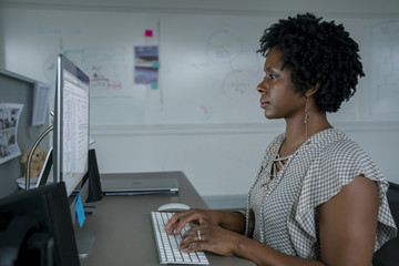 Side view of businesswoman using desktop computer while sitting at desk in office