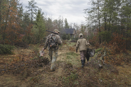 Rear view of boy carrying dead turkey while walking with father on field
