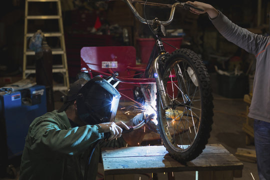 Father and son welding tricycle in workshop