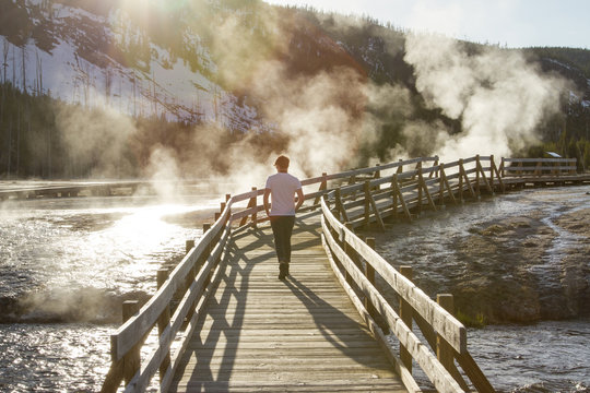 Rear view of hiker walking on boardwalk by hot springs at Yellowstone National Park
