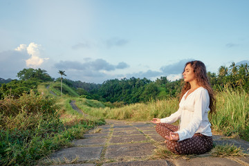 Yoga at Campuhan Ridge Walk, Bali Island. Young woman in lotus pose sitting on path. Concept of calm and meditation.