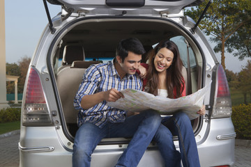 Young man and young woman sitting in the trunk of a car