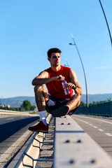 Portrait of young athlete man resting after running and drinking water on bridge.
