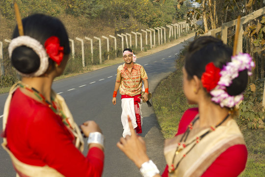 Bihu dancers look on as a Bihu man walks up to them 