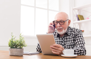 Senior man talking on phone with tablet