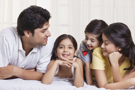 Family looking at little girl while lying in bed 