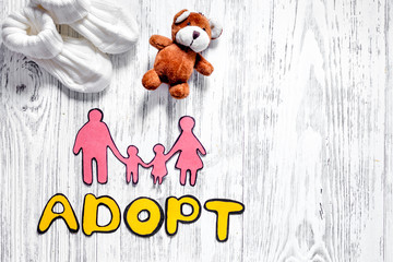 Adopt word, paper silhouette of family and toys on light wooden table background top view copyspace