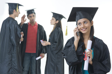 Happy graduate student answering mobile phone with friends discussing over white background