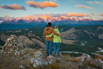 Fototapeta premium Tourist couple - girl and guy embracing and enjoying beautiful mountain landscape with morning haze over the mountains and forests. Panorama