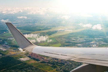 View of the wing of the plane in the porthole on the city and the airport with picturesque clouds