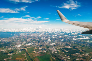 Naklejka na ściany i meble View of the wing of the plane in the porthole on the city and the airport with picturesque clouds