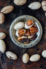 Pecan nuts on metal plate over black rustic surface.
