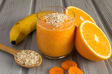 Smoothie from banana, orange,carrot and oat flakes on the grey wooden background 