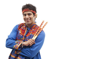 Portrait of happy young man in traditional wear holding dandiya over white background