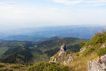Mountain view with young woman sitting on top. Tourism concept background.