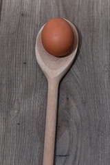 One egg on a wooden spoon on top of a wooden table