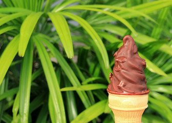 Front View of Chocolate Dipped Soft Serve Ice Cream Cone, Blurred Green Foliage in Background 